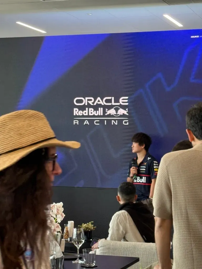 yuki tsunoda holding a microphone in front of a red bull racing screen