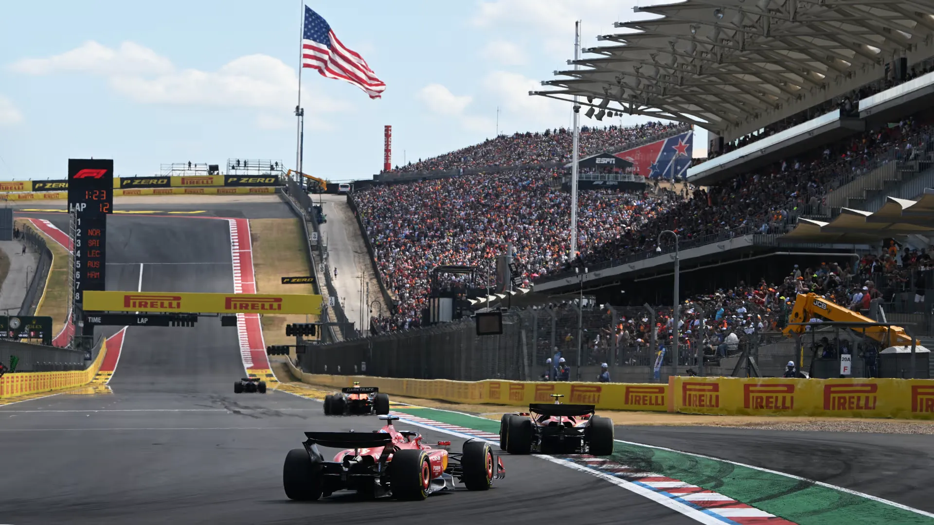 two ferraris climb the hill at the circuit of the americas in front of packed grandstands and a US flag