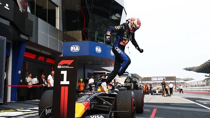 max verstappen jumps off his red bull next to the number 1 board after winning at sepang