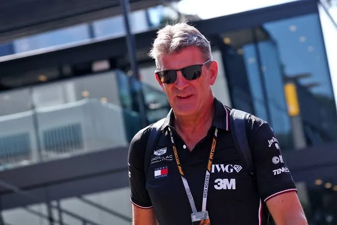 graeme lowdon in a black cadillac team shirt and sunglasses, walking through the paddock