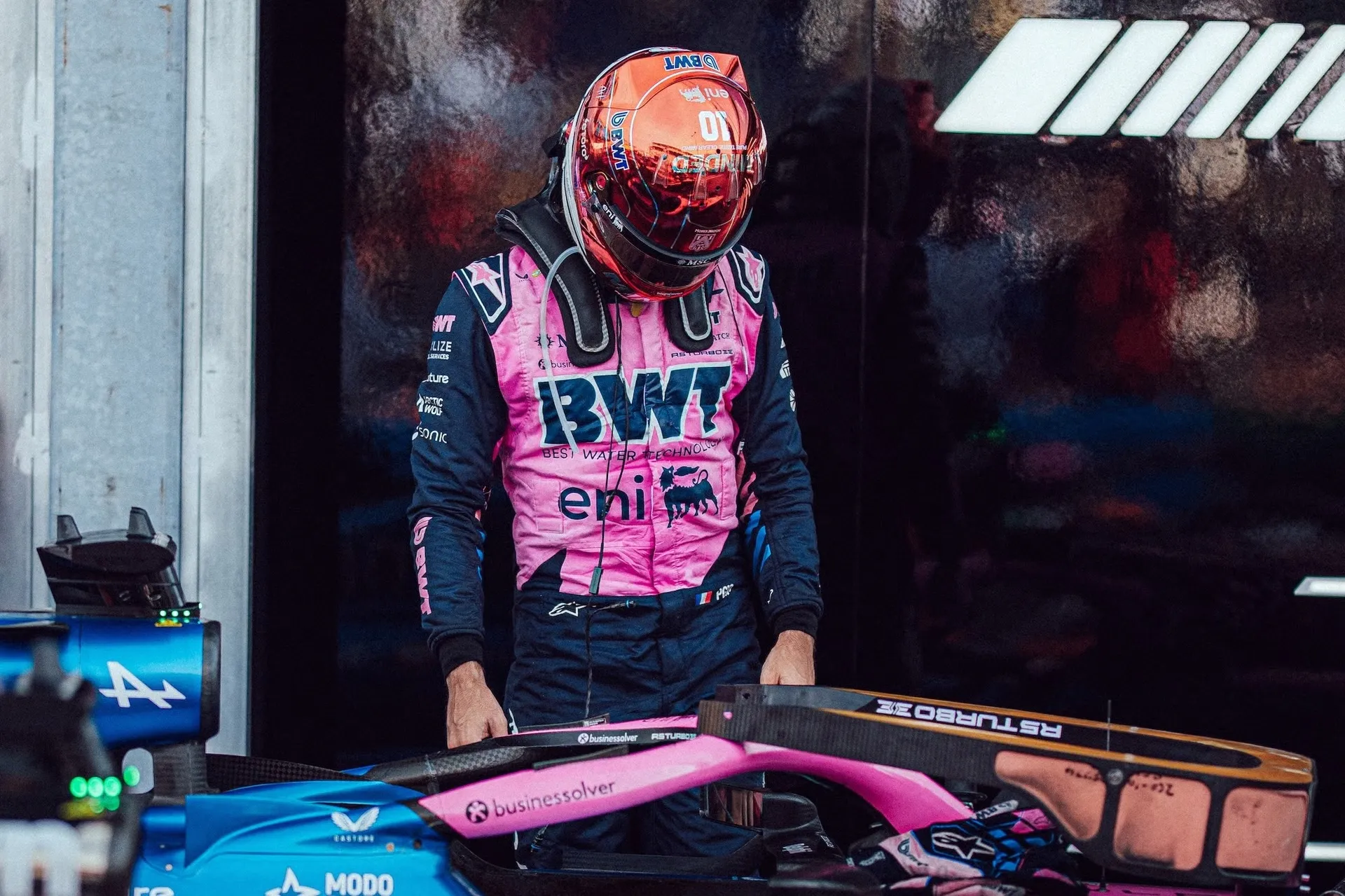 pierre gasly in his pink alpine race suit and helmet, looking down at his car