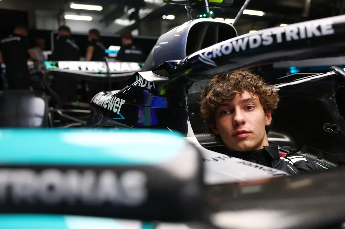 a mercedes driver sits in the car in the team garage, looking at the camera