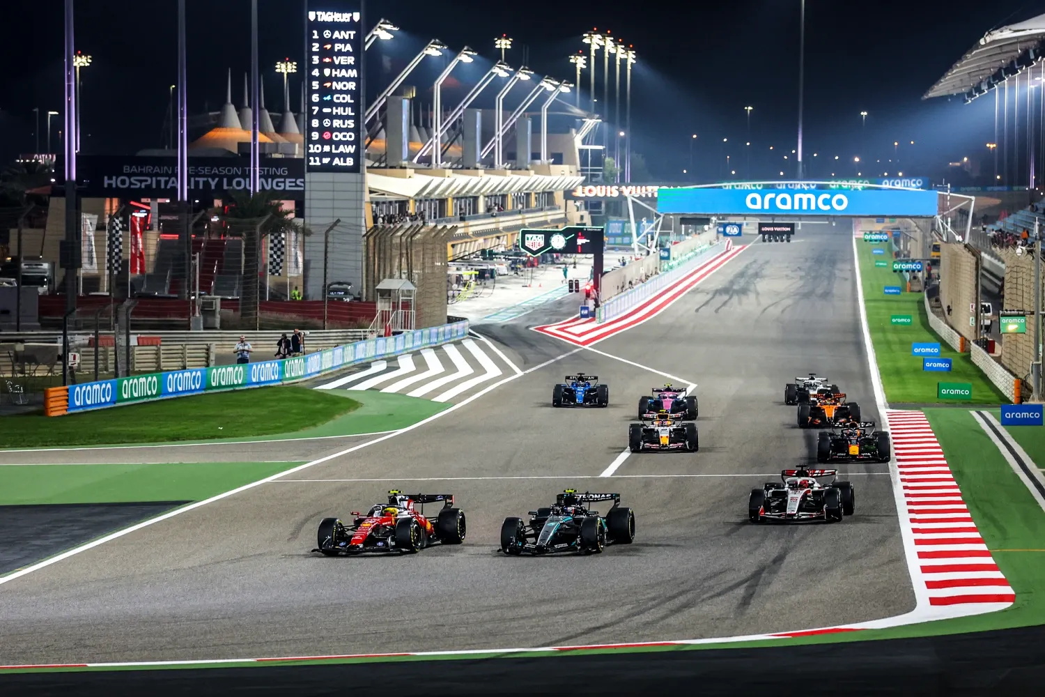 the start of a night race seen from above, the cars fanning out across the track