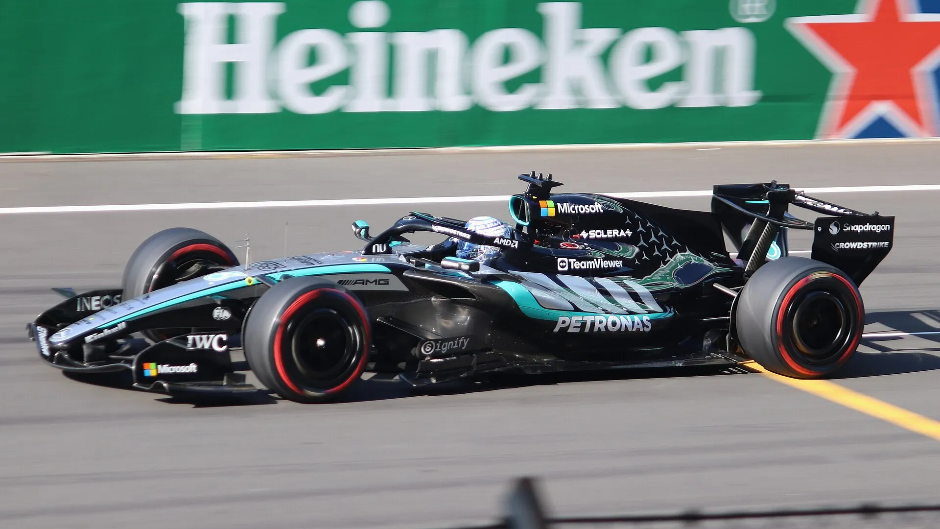 george russell's mercedes at speed in front of a trackside advertising board