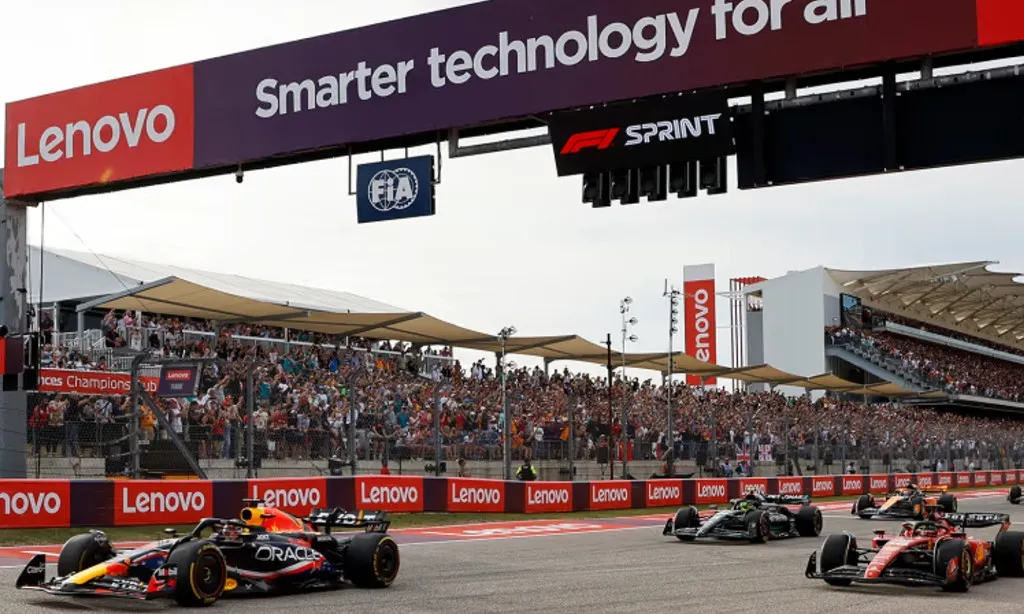 a red bull leads a mercedes and a ferrari under the start gantry at austin, the grandstand full behind them